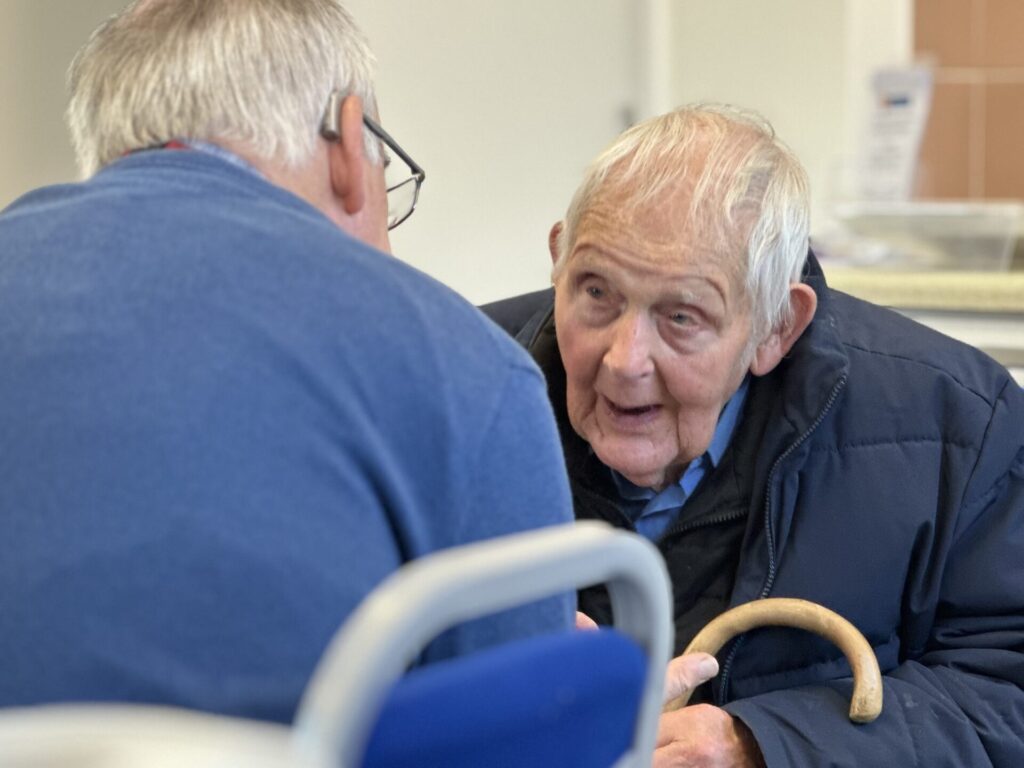 A CDA volunteer in conversation with an older man at a Hearing Help drop-in session