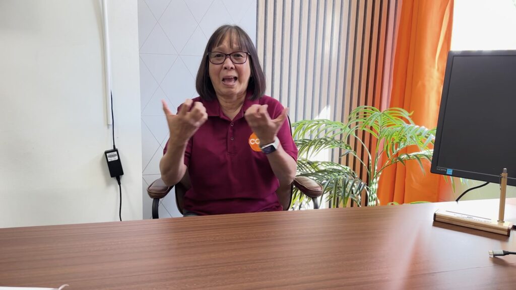 Ky from Cambridgeshire Deaf Association signing in BSL at a desk