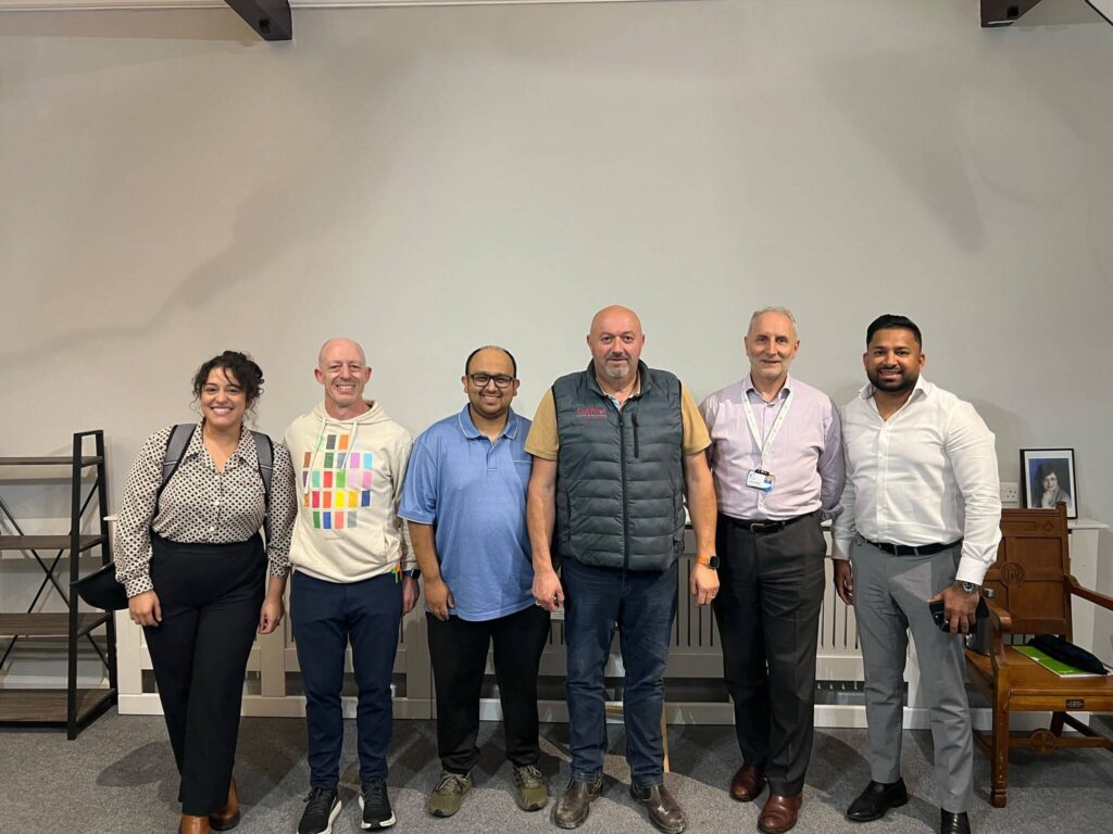Six people from the Mill Road Traders’ Association workshop standing together in the hall at CDA’s Cambridge office on Romsey Terrace