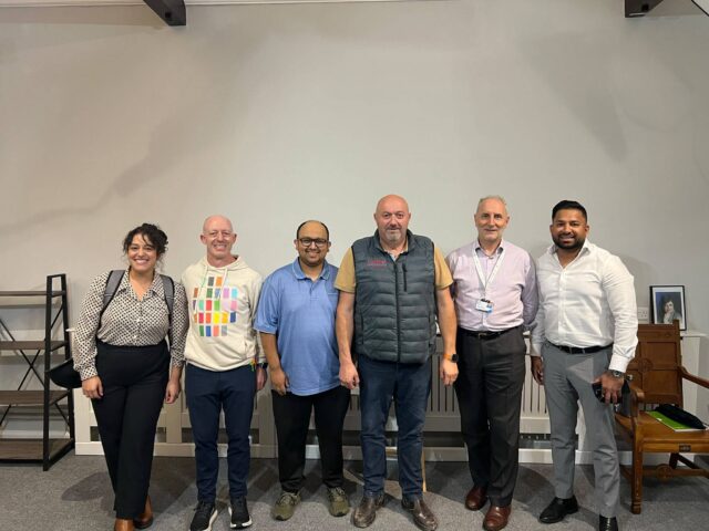 Six people from the Mill Road Traders’ Association workshop standing together in the hall at CDA’s Cambridge office on Romsey Terrace